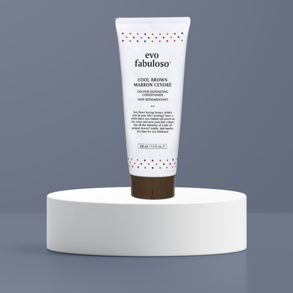 A white tube of evo fabuloso Cool Brown Marron Cendré skin restorative cream, standing upright on a white cylindrical pedestal against a slate gray background.